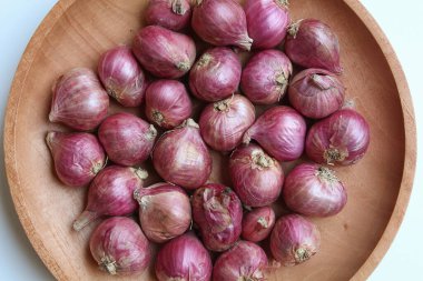 Red onion or shallots, on wooden plate, isolated on white background clipart