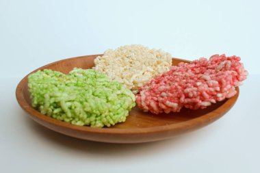 Rengginang, traditional crackers from Indonesia, made from sticky rice which dried then fried. White, green and red olor. On a wooden plate, isolated on white background clipart