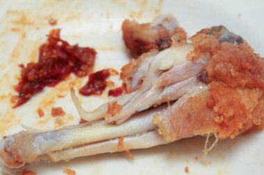 Yemek artıkları ya da yiyecek atıkları. Tabakta kızarmış tavuk ve acı biber sosu var.