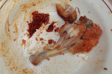 Yemek artıkları ya da yiyecek atıkları. Tabakta kızarmış tavuk ve acı biber sosu var.