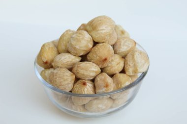 Dried Indonesian Candlenuts, or Kemiri, the seed of Aleurites moluccanus inside a transparant bowl, isolated in white background clipart