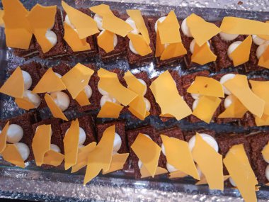 Tatlı barında ısırık büyüklüğünde pasta. Üzerinde beyaz krema ve sarı renkli çikolata olan çikolatalı pasta.