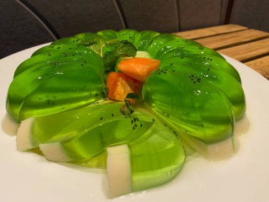 Beyaz tabakta servis edilen yeşil kavun pudingi.