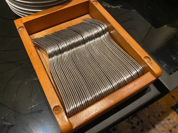 Siyah masanın üzerinde tahta bir kutuda metal çatallar var.