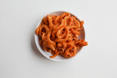 Kırmızı renkli baharatlı kızarmış şehriye, küçük beyaz bir kase, beyaz arka planda izole, düz ya da üst görünümde.