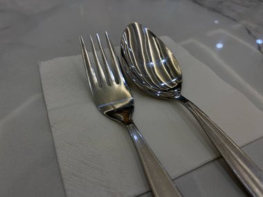 Bir set paslanmaz çelik kaşık ve çatal, beyaz masanın üstünde.