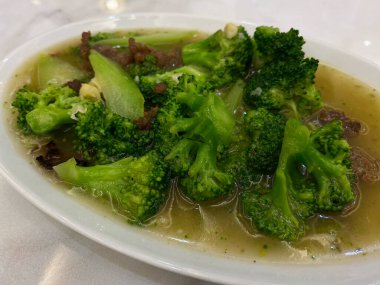 Brokoliyi kahverengi soslu, sığır etini beyaz tabakta, beyaz mermer masada karıştır.