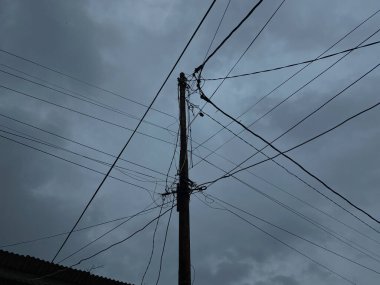 Power supply pole and cables, with dark cloudy sky background clipart