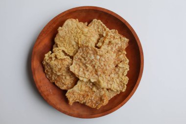 Keripik tempo veya tempeh krakerleri, kare şeklinde. İnce dilimler, un hamuruyla kızartılmış tempeh. Tahta tabakta, beyaz arkaplanda izole edilmiş, düz ya da üst görünümde