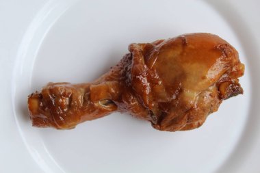 Ayam Kkapap, ya da tatlı soya sosuyla pişirilmiş tavuk. Beyaz tabakta bir tavuk budu, beyaz arka planda izole, düz ya da üst görünümde