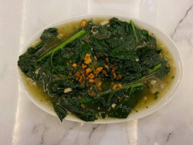 Beyaz tabakta, beyaz masada sarımsaklı ve koyu kahverengi soslu gai lan kızartması. Gai lan, kai lan, Çin brokolisi, Çin lahanası, ya da Brassica oleracea var. alboglabra