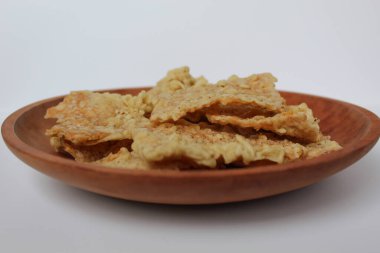 Keripik tempo veya tempeh krakerleri, kare şeklinde. İnce dilimler, un hamuruyla kızartılmış tempeh. Tahta tabakta, beyaz arka planda izole edilmiş.