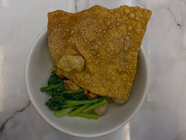 Endonezya köftesi, kızarmış hamur köftesi, sebze olarak yeşil hardal yaprağı, et suyu olmadan servis edilir. Beyaz kase, beyaz mermer masa, üst ya da düz yatıyordu