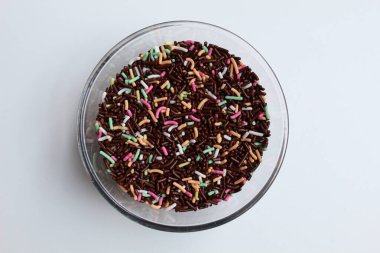 Şeffaf cam kasede renkli çikolata parçacıkları, beyaz arka planda izole, düz ya da üst görünümde