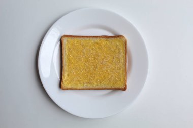 Bir dilim beyaz kare ekmek, margarin yayılmış ve beyaz kristal şeker kaplı, beyaz zemin üzerinde izole, düz ya da üst görünüm