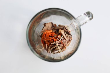 Wedang Uwuh, ya da Java bitkisel içeceği, transparante bardağın içinde, beyaz arka planda, düz yerde ya da üst tarafta izole edilmiş. Hintli kızılağaç, kuru zencefil, limon otu ve kakule karışımından önce hazırlanan malzemeler.