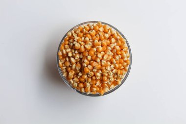 Cam şeffaf kâse ile dolu kurumuş mısır taneleri, beyaz arka planda izole edilmiş, düz ya da üst görünüm