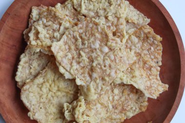 Keripik tempo veya tempeh krakerleri, kare şeklinde. İnce dilimler, un hamuruyla kızartılmış tempeh. Tahta tabakta, beyaz arkaplanda izole edilmiş, düz ya da üst görünümde