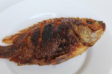 Beyaz bir tabakta kızarmış gurami balığı, beyaz arka planda izole edilmiş.