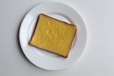 One slice of white square bread, with margarine spread, on white plate, isolated on white background, flat lay or top view clipart