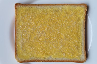 Bir dilim beyaz kare ekmek, margarin yayılmış ve beyaz kristal şeker kaplı, beyaz zemin üzerinde izole, düz ya da üst görünüm