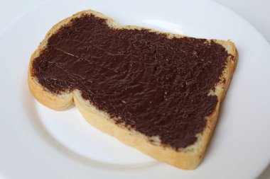 Bir dilim beyaz ekmek, çikolata ile kaplanmış, beyaz tabakta, beyaz arka planda izole edilmiş. Çikolatalı sandviç hazırla.