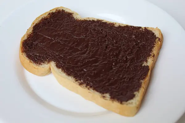 Bir dilim beyaz ekmek, çikolata ile kaplanmış, beyaz tabakta, beyaz arka planda izole edilmiş. Çikolatalı sandviç hazırla.