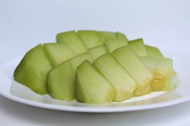 Küçük kesikler yeşil kavunlar ya da kavunlar, beyaz tabakta, beyaz arka planda izole edilmiş.