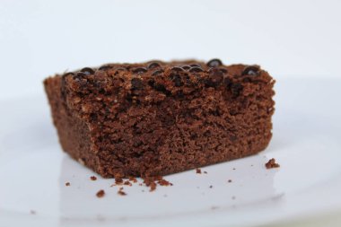 Kare şeklinde çikolatalı kek. Üstünde çikolata parçaları var. Beyaz arka planda izole edilmiş.