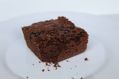 Kare şeklinde çikolatalı kek. Üstünde çikolata parçaları var. Beyaz arka planda izole edilmiş.