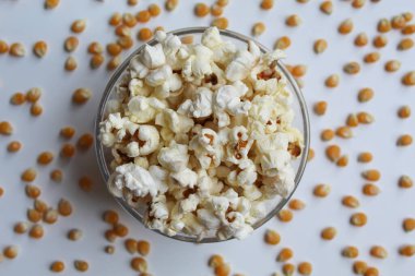 Bir kase patlamış mısır ve etrafa saçılmış mısır tohumu çekirdekleri, beyaz arka planda izole, düz ya da üst görünüm