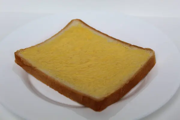 Beyaz arka planda izole edilmiş, beyaz tabakta margarin serpiştirilmiş bir dilim beyaz kare ekmek.