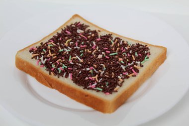 Beyaz arka planda izole edilmiş, renkli çikolata parçacıkları serpiştirilmiş bir dilim beyaz kare ekmek.