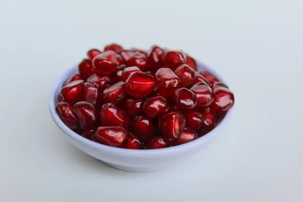 Nar meyvesinden taze kırmızı tohumlar, küçük kasede, beyaz arka planda izole edilmiş.