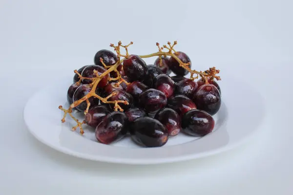 Koyu mor ya da siyah üzüm, saplı, beyaz plakalı, beyaz arka planda izole edilmiş.