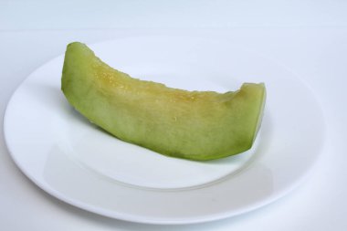 Bir kesik yeşil kavun ya da kavun, beyaz tabakta, beyaz arka planda izole edilmiş.