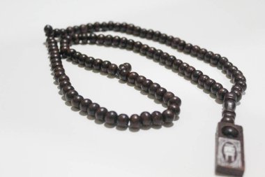 İslami dua boncukları koyu kahverengi renklerde, birbirine dolanmış, beyaz arka planda izole edilmiş.