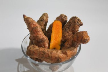 Turmeric or Curcuma longa rhizomes in a bowl, isolated in white background. Whole pieces and peeled piece, visible flesh clipart