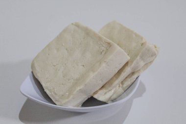Küçük bir kasede iki parça ipeksi süt tofu, pişmemiş, beyaz arka planda izole edilmiş.