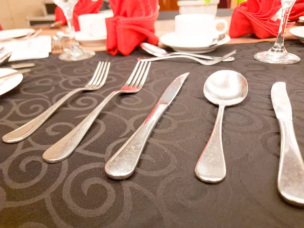 Gümüş metal kaşık, gümüş metal çatal, kırmızı peçete, siyah masa örtüsü.