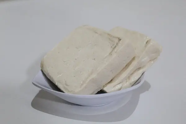 Küçük bir kasede iki parça ipeksi süt tofu, pişmemiş, beyaz arka planda izole edilmiş.