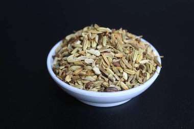 Dried granules of Aniseed, or Pimpinella Anisum seed, or Adas Manis, inside a bowl. Isolated on black background clipart