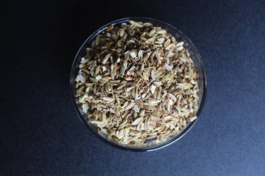 Dried granules of Aniseed, or Pimpinella Anisum seed, or Adas Manis, inside a bowl. Isolated on black background. Flat lay or top view clipart