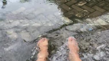 Sığ bir nehirde çıplak ayakla dolaşan bir kadın. Gri asfaltlı berrak suya daldırılmış ayak