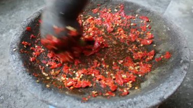 Asyalı bir el kırmızı biber ve kireçle taş havan ve tokmakla vuruyor. Bir Endonezya yemek çeşnisi olan sambal yapma süreci
