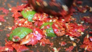Asyalı bir el kırmızı biber ve kireçle taş havan ve tokmakla vuruyor. Bir Endonezya yemek çeşnisi olan sambal yapma süreci