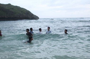 Asyalı çocuklar dalgaların arasında eğleniyor. 8 Ekim 2022 'de Yogyakarta, Endonezya