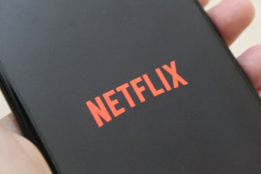 Netflix uygulama logosu siyah arkaplanı olan bir akıllı telefon üzerinde. Netflix, küresel bir dizi ve film sağlayıcısıdır. Telefon elle tutuluyor. 27 Kasım 2022 'de Semarang, Endonezya