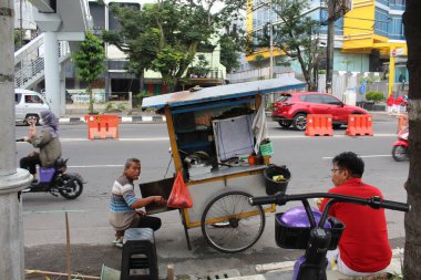 Arabası olan bir adam sigara içerken yemek satar. 12 Nisan 2022 'de Semarang, Endonezya