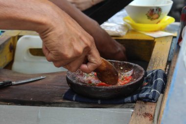 Asyalı bir el ahşap havan ve tokmakla acı biber ve arpacık soğanı eziyor.